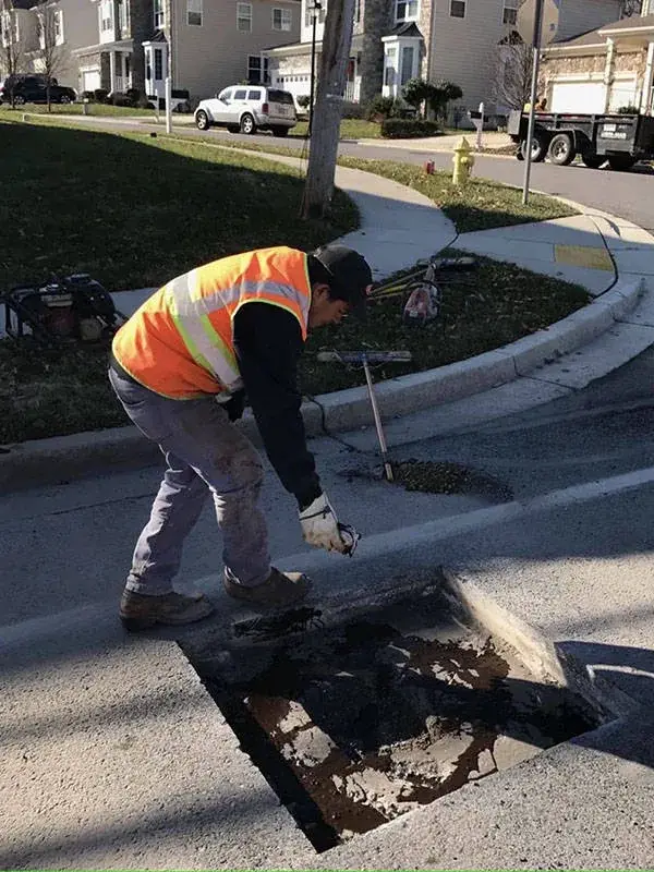 A worker in high-visibility clothing cutting out a failed section of asphalt for patching