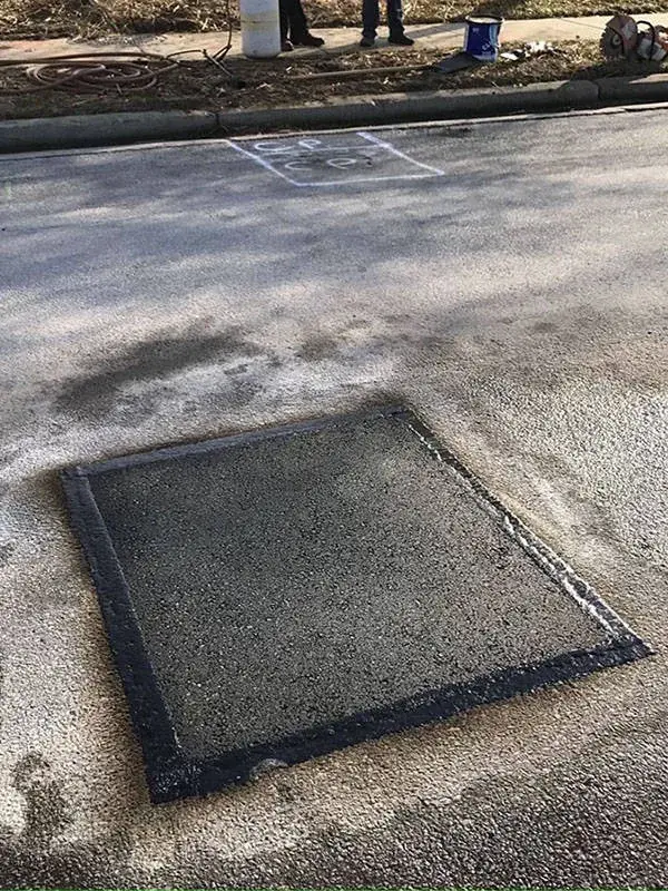 A completed square asphalt patch sealed flush into the surrounding pavement