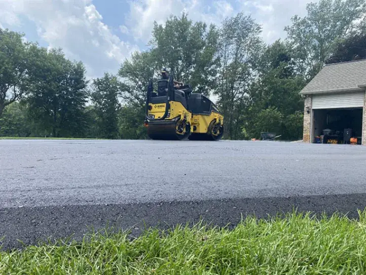 A double-drum roller compacting a newly laid asphalt driveway