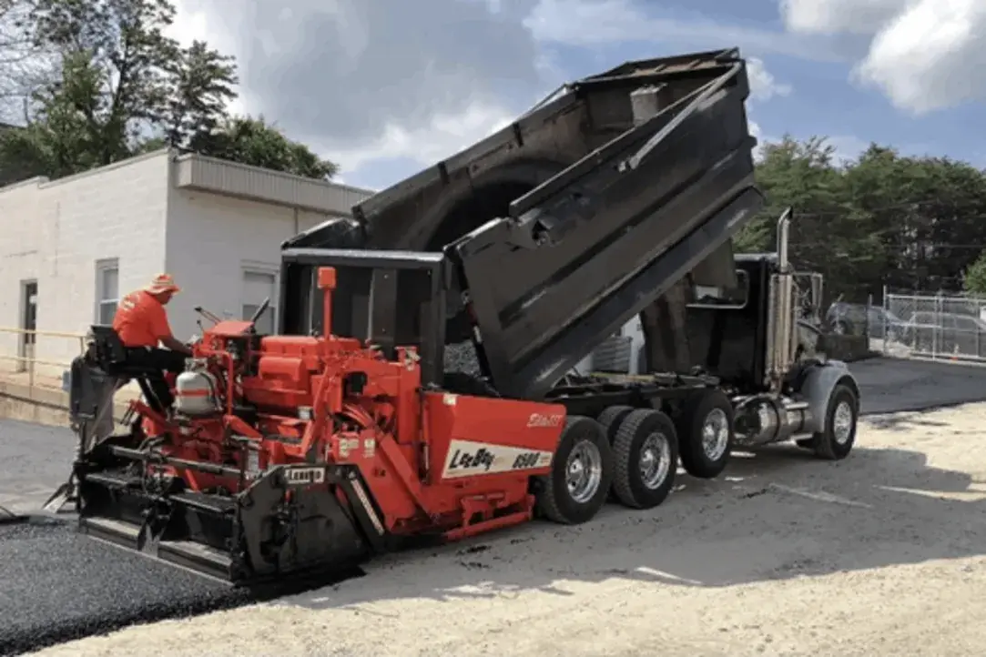 A paving crew working behind a paver and dump truck on a commercial lot