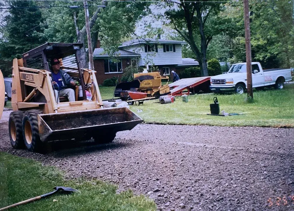 A skid steer grading the gravel base of a residential driveway before paving