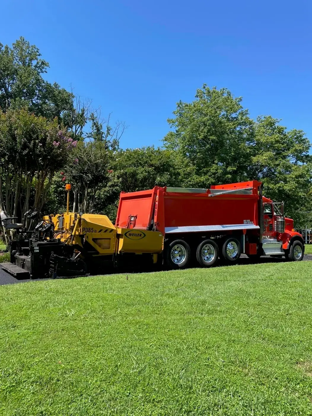 An All Star paver and dump truck working at the edge of a residential lawn