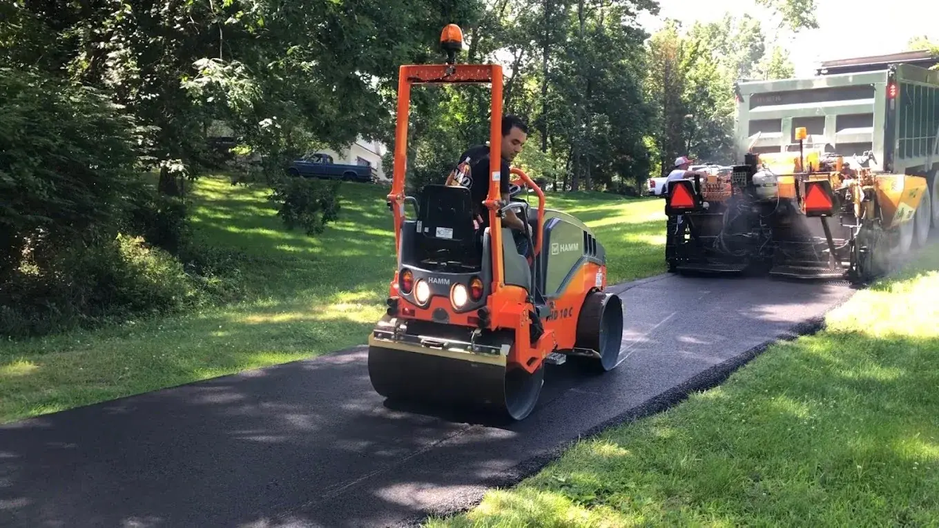 A compact roller compacting a freshly laid asphalt driveway, with the paver still working behind it