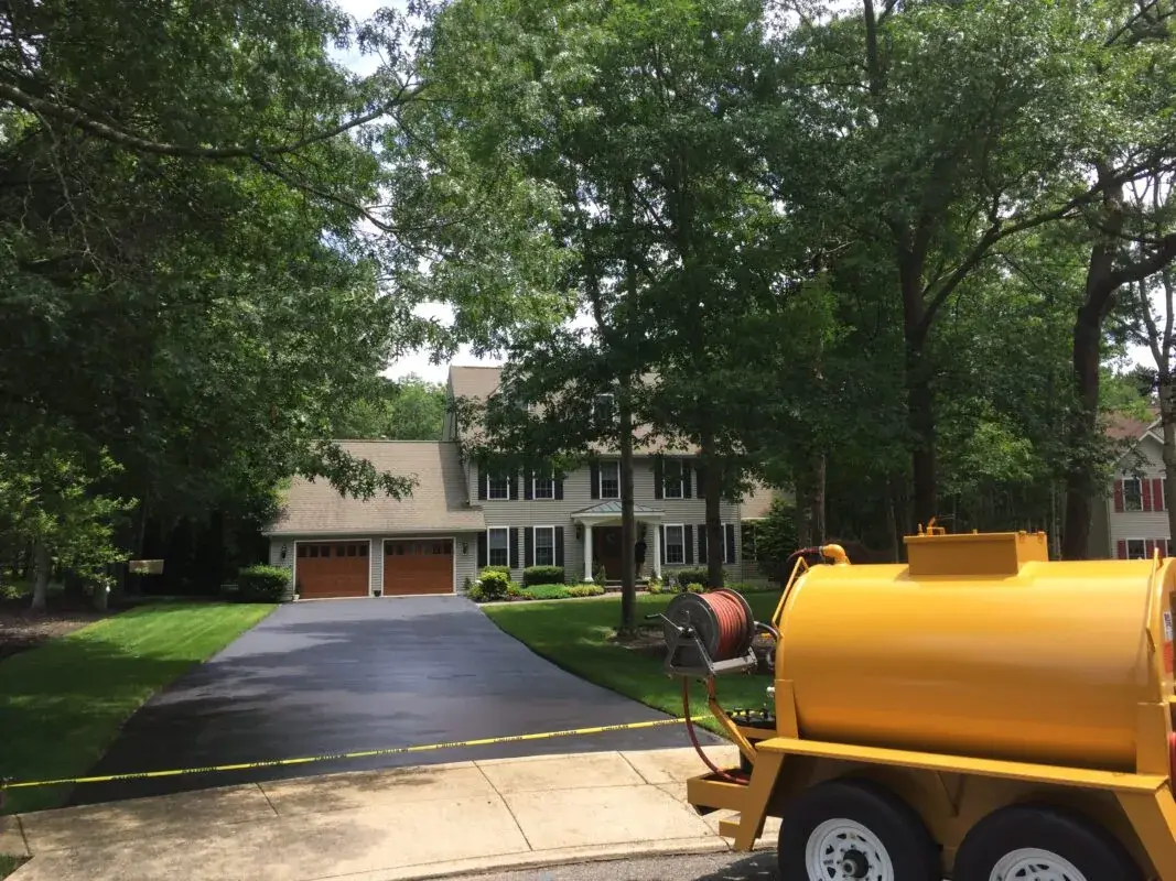 A sealcoat tank trailer parked at the foot of a freshly sealed residential driveway