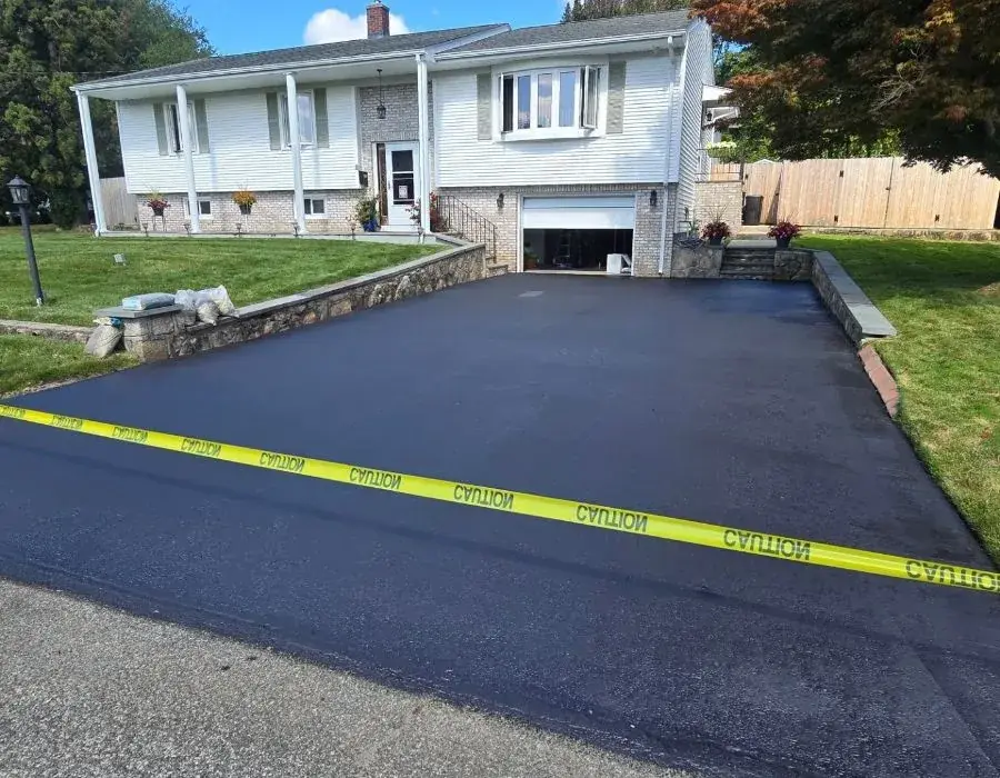 A freshly sealcoated residential driveway leading up to a house, taped off while it cures